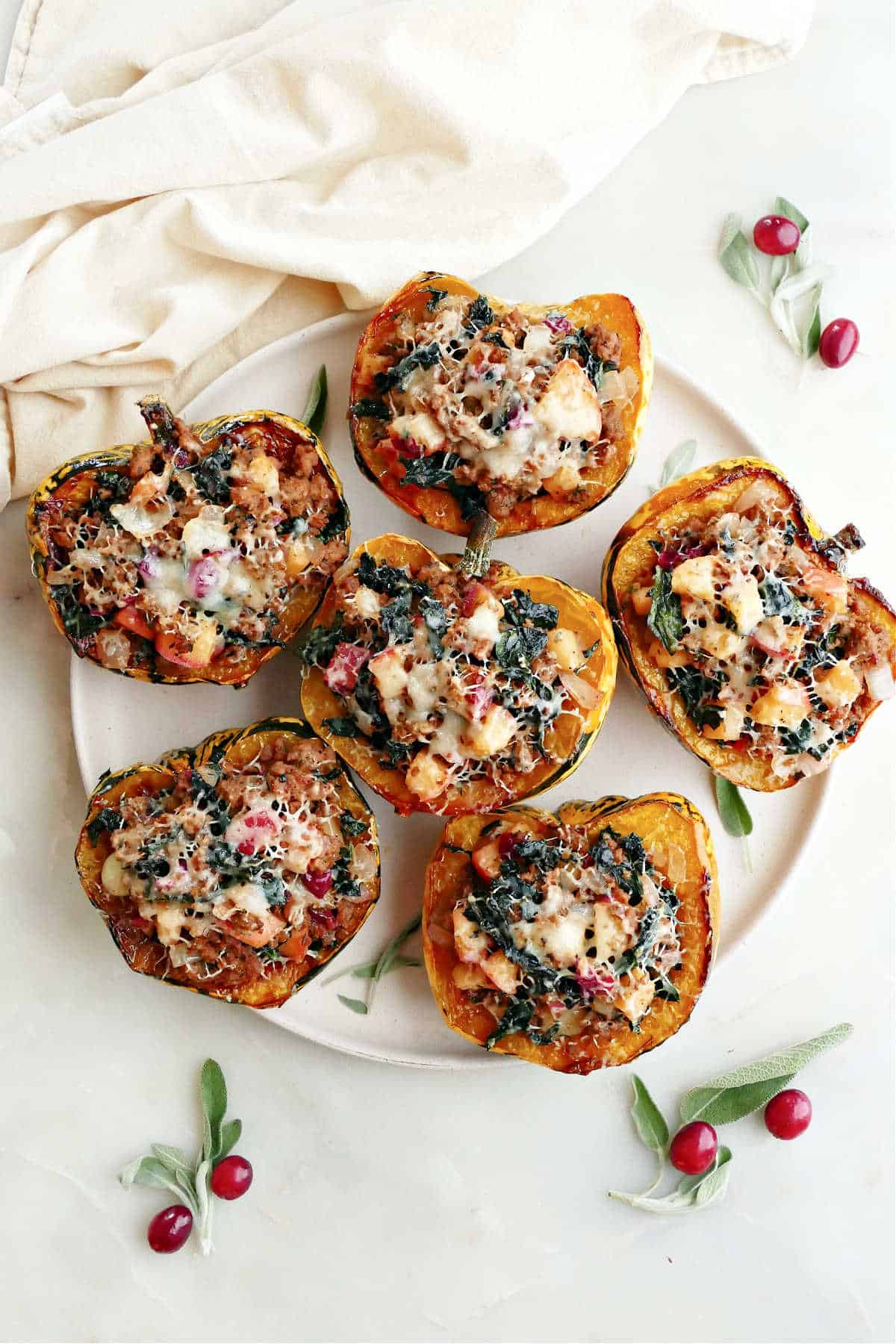 Six stuffed carnival squash on a platter on a counter next to a napkin and garnish.