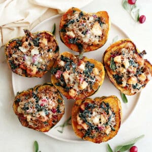 Six stuffed carnival squash on a platter on a counter next to a napkin and garnish.