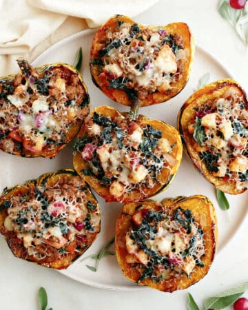 Six stuffed carnival squash on a platter on a counter next to a napkin and garnish.
