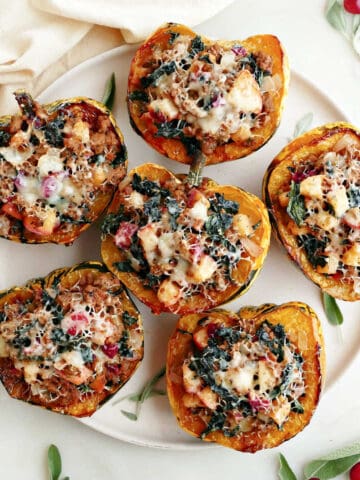 Six stuffed carnival squash on a platter on a counter next to a napkin and garnish.