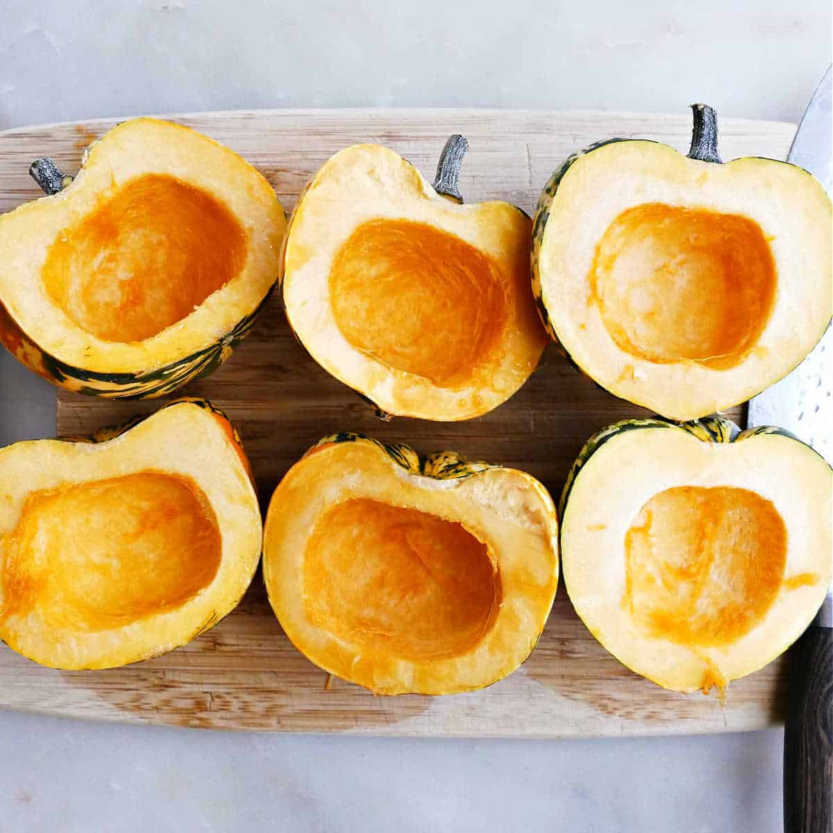 Six carnival squash halves with seeds scooped out on a cutting board.