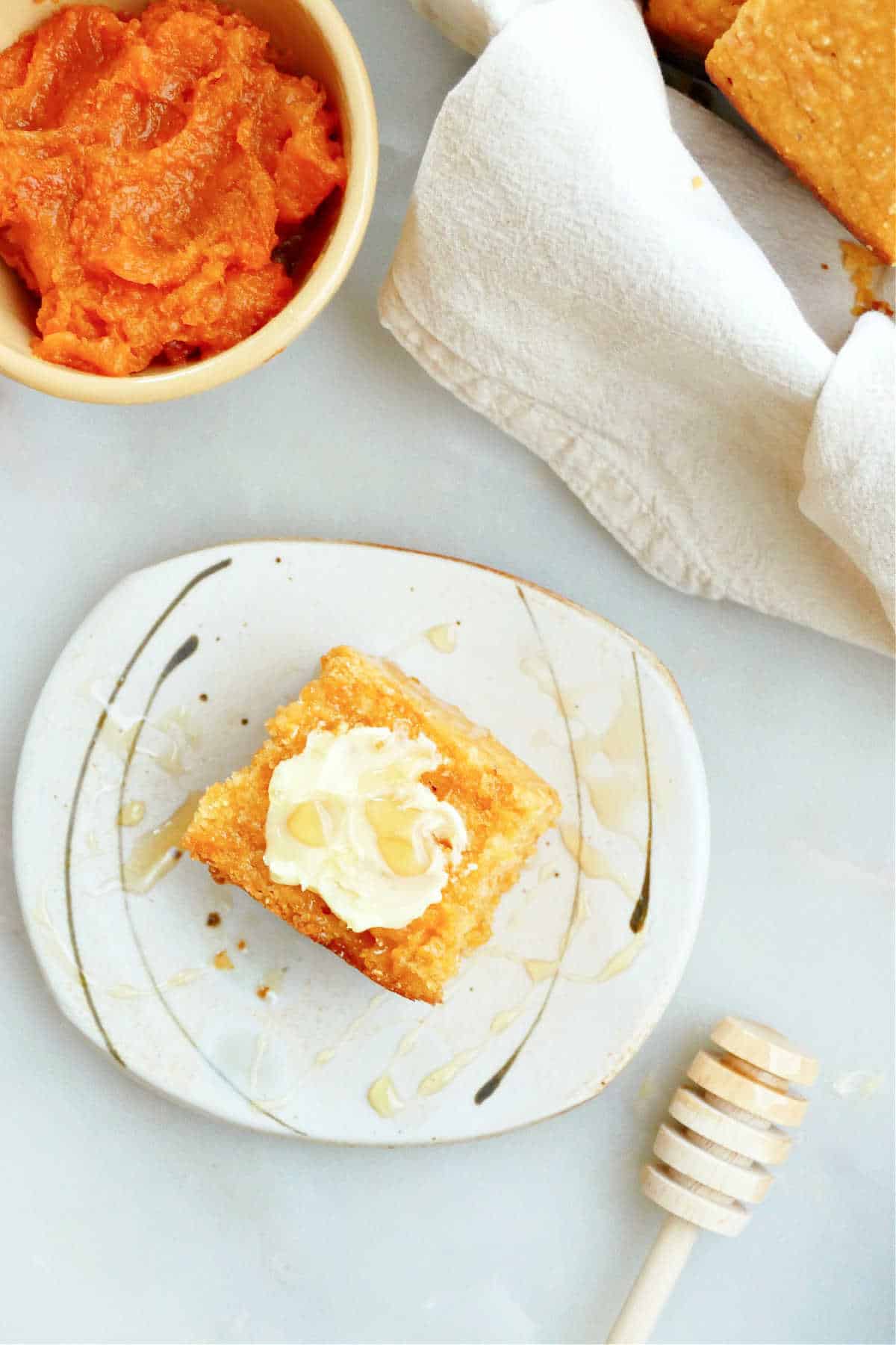 A square of sweet potato cornbread on a small plate topped with butter and drizzled with honey.