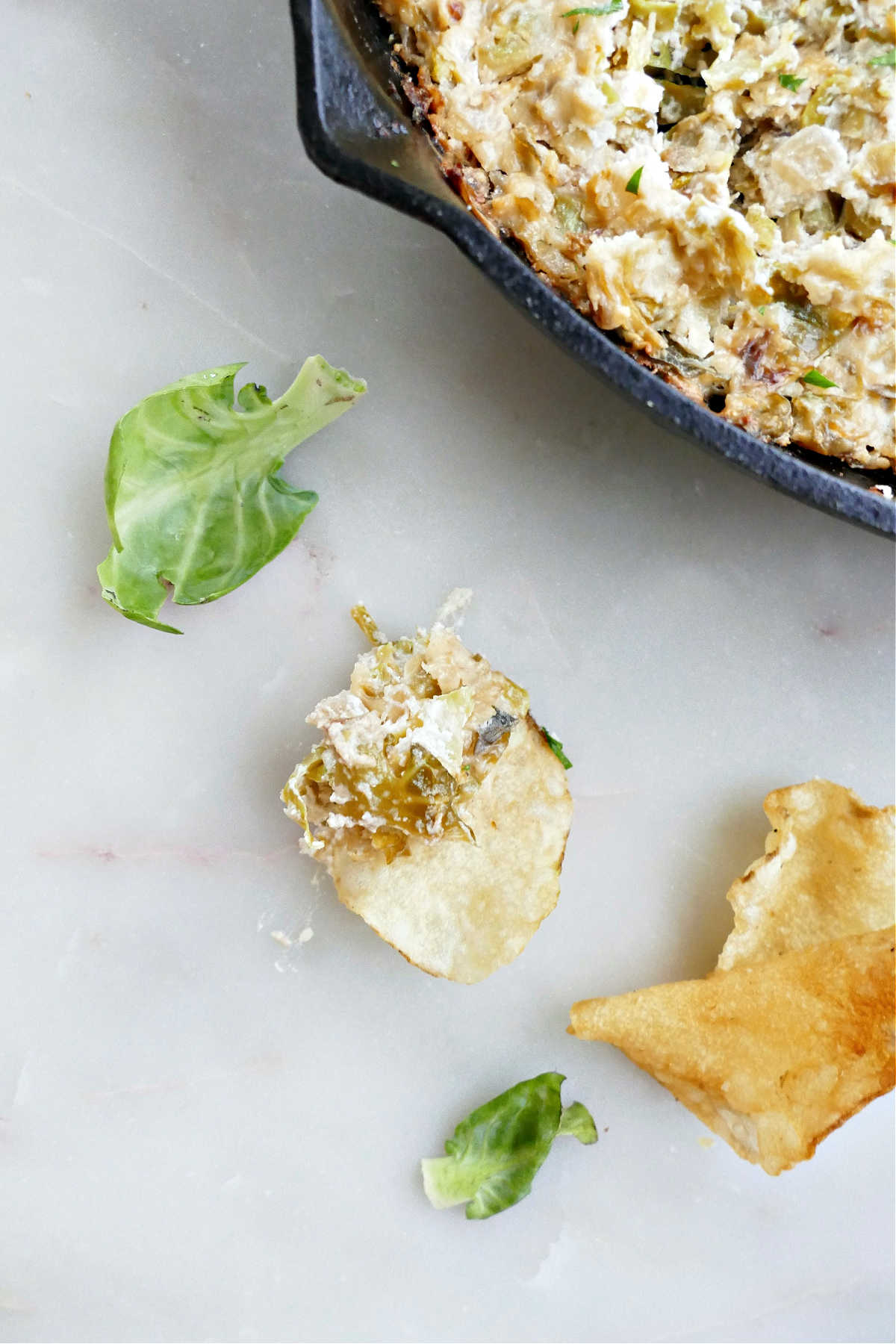 A potato chip with Brussels sprouts dip on a counter.