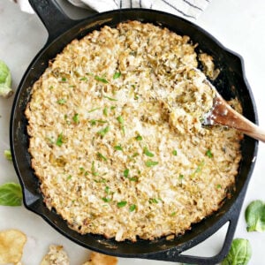 Brussels sprouts and cheese dip in a cast iron skillet with a spoon next to chips and Brussels sprouts.