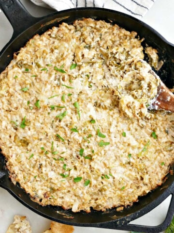 Brussels sprouts and cheese dip in a cast iron skillet with a spoon next to chips and Brussels sprouts.