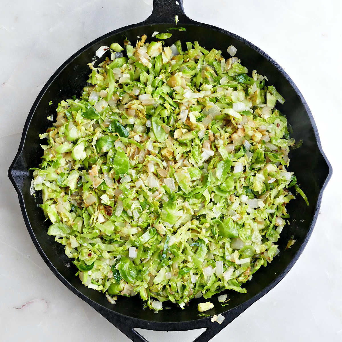 Brussels sprouts, onion, and garlic cooking in a cast iron skillet.