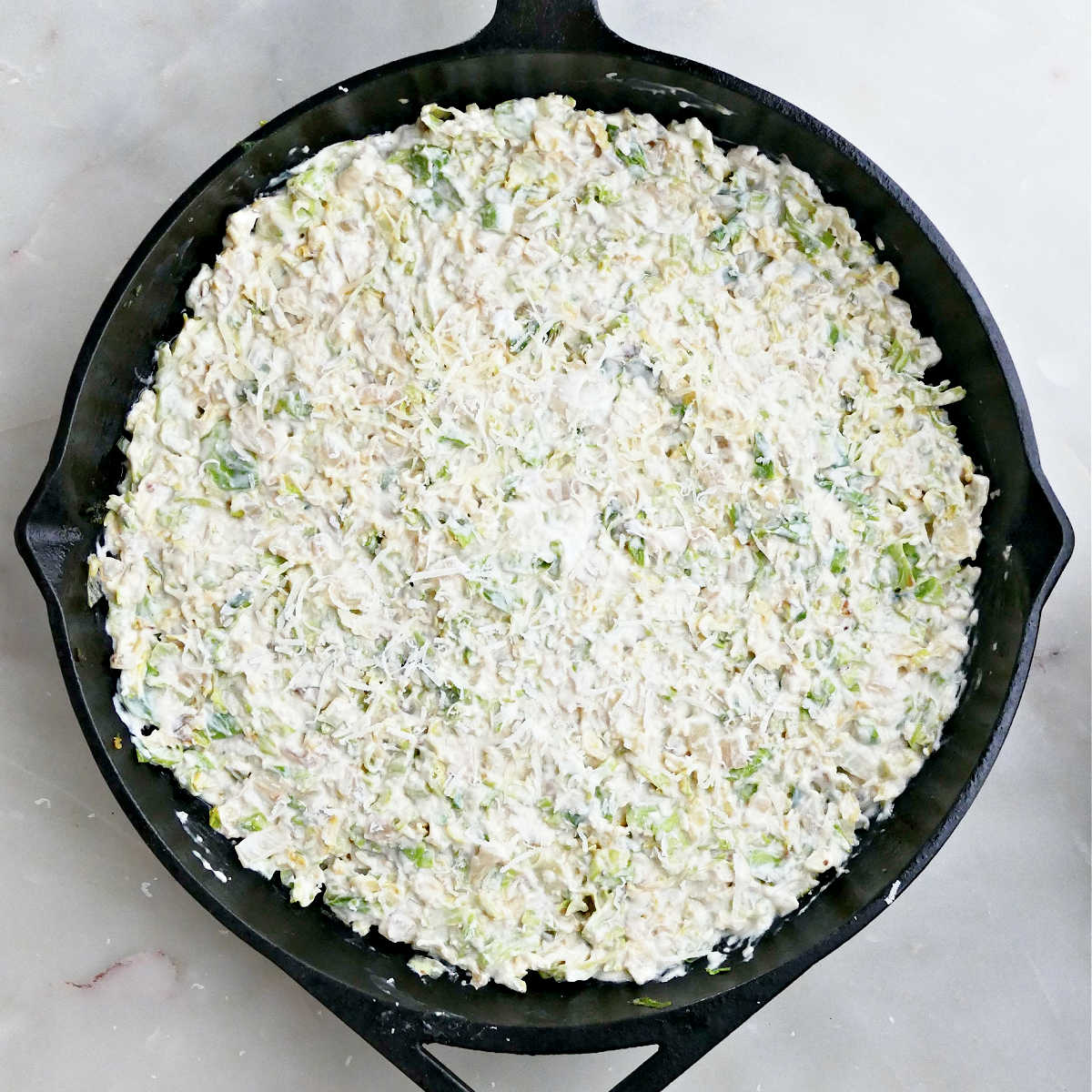 Brussels sprouts dip spread out in a cast iron skillet before going into the oven.