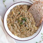 Lentil bake in a bowl with a piece of bread next to garnishes and more bread.