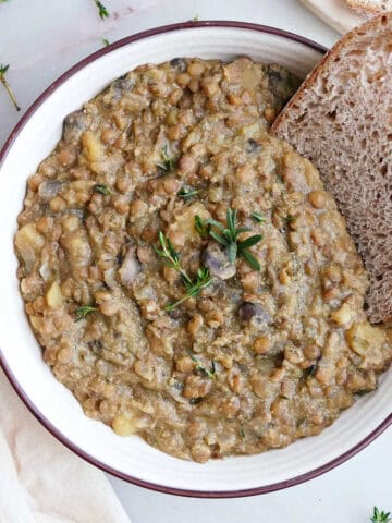 Lentil bake in a bowl with a piece of bread next to garnishes and more bread.