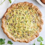 Loaded vegetarian quiche next to gruyere cheese, parsley, eggs, and napkin.