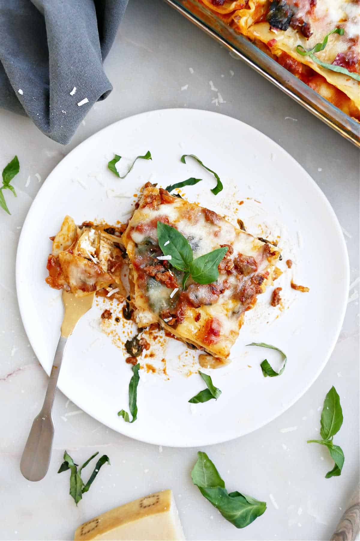 Slice of beef spinach lasagna with a fork and basil garnish on a plate.