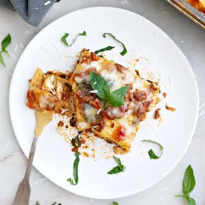 Slice of beef spinach lasagna with a fork and basil garnish on a plate.