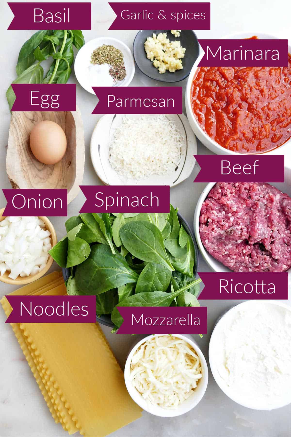 Ingredients for lasagna in bowls on a counter with labels.