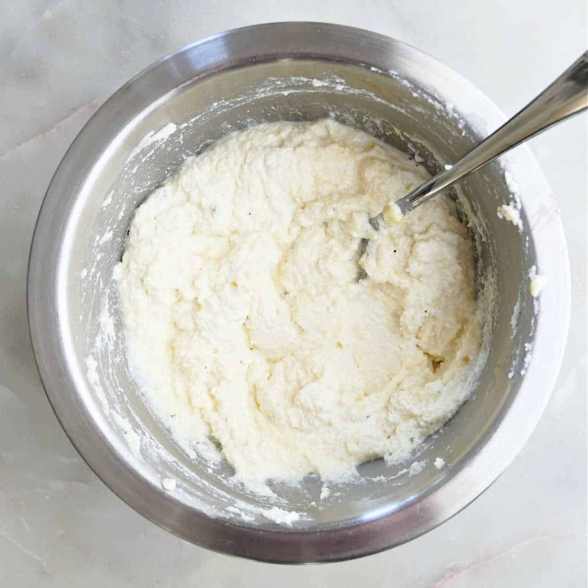 Ricotta cheese mixed with an egg and seasonings in a bowl.