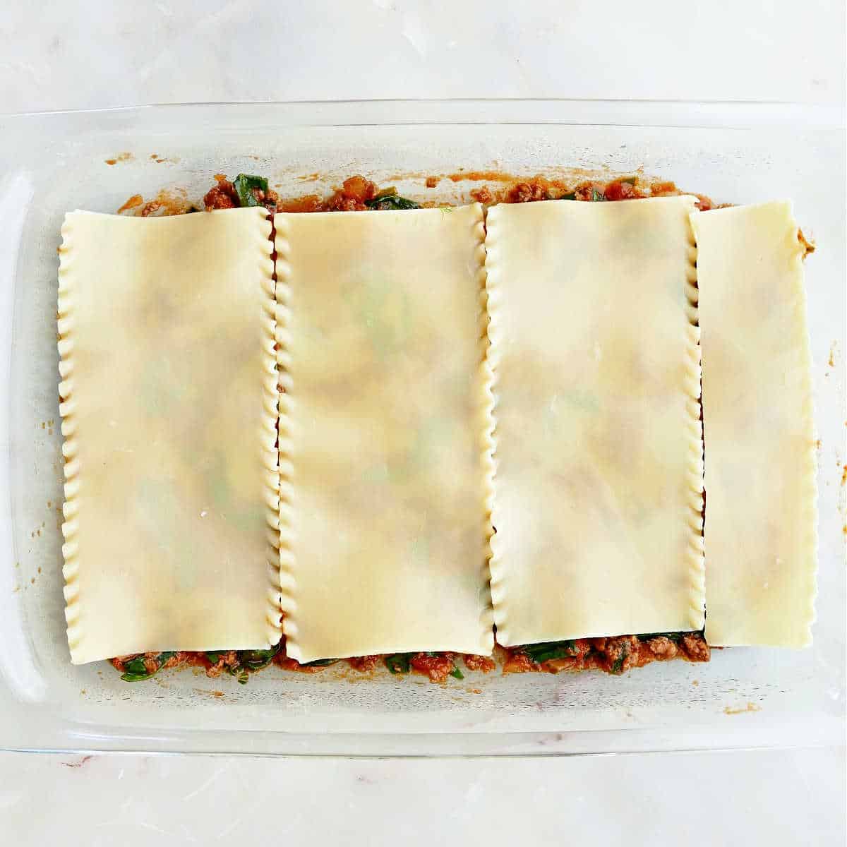 A layer of sauce covered by lasagna noodles in a baking dish.