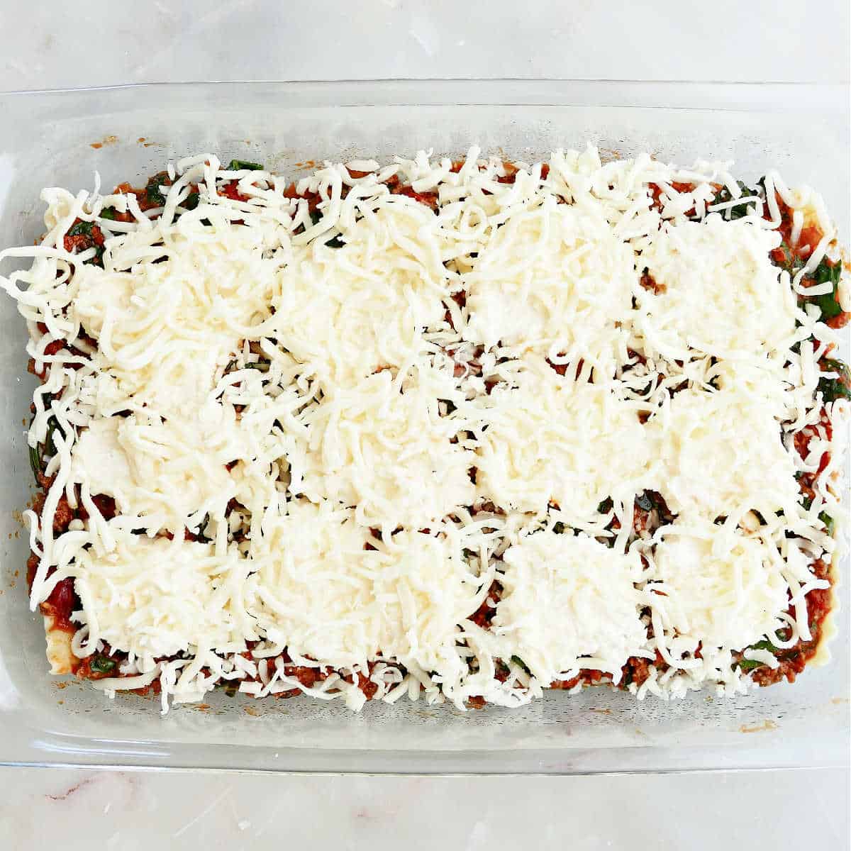 Lasagna layers covered with shredded cheese in a pan before baking.