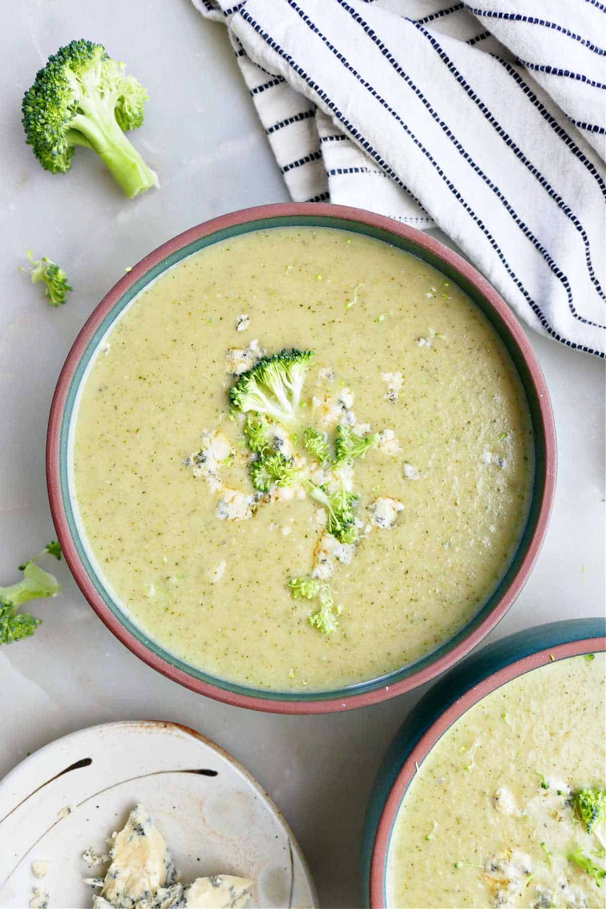 Broccoli and blue cheese soup in a bowl next to toppings and a napkin.