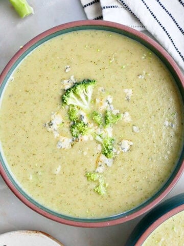 Broccoli and blue cheese soup in a bowl next to toppings and a napkin.