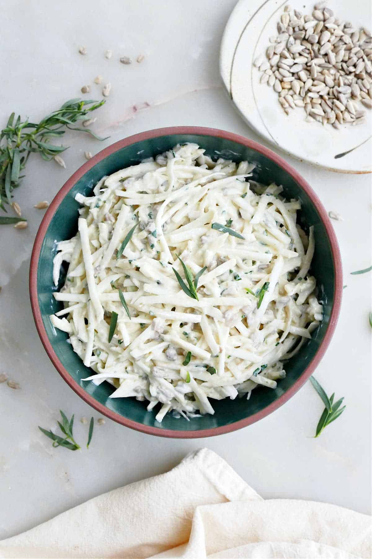 Celeriac coleslaw in a bowl on a table surrounded by garnishes.