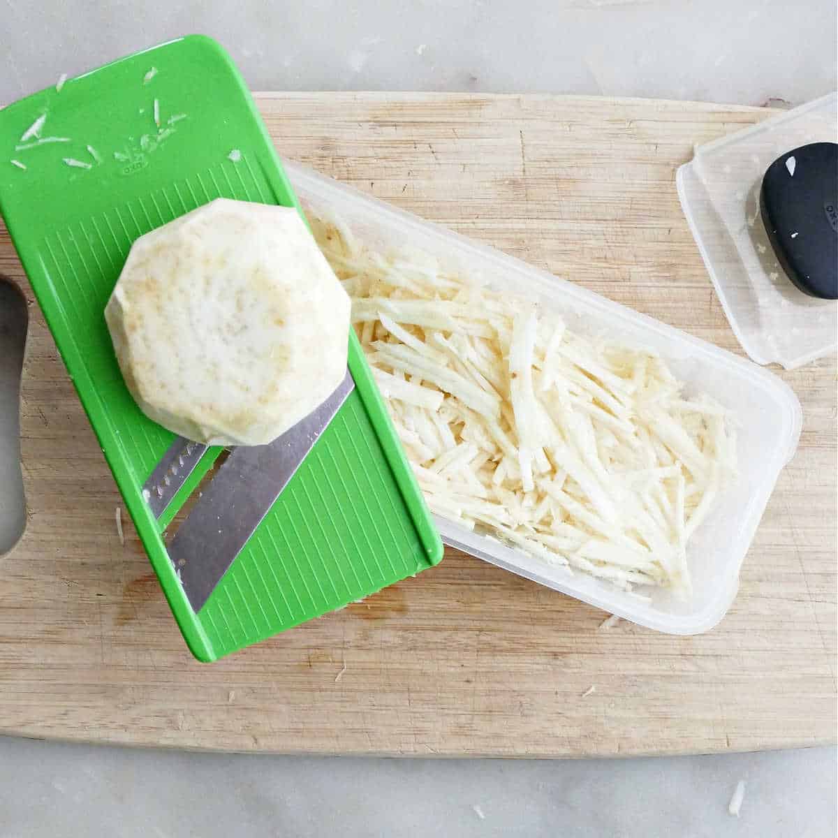 Celery root being grated into matchsticks using a slicing tool.