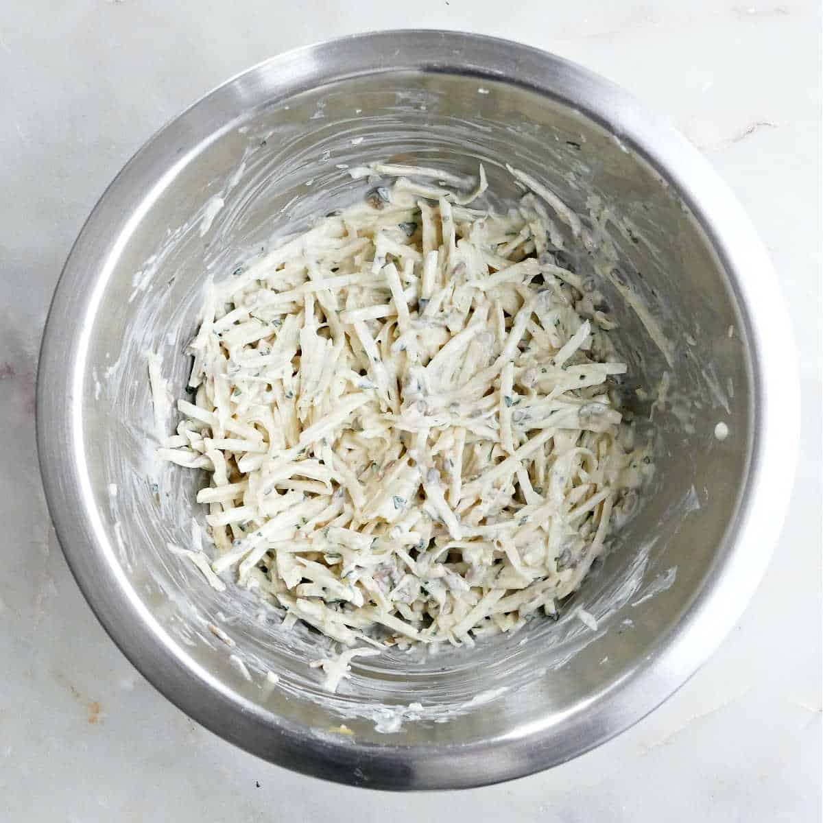 Celeriac slaw after being coated with dressing in a mixing bowl.