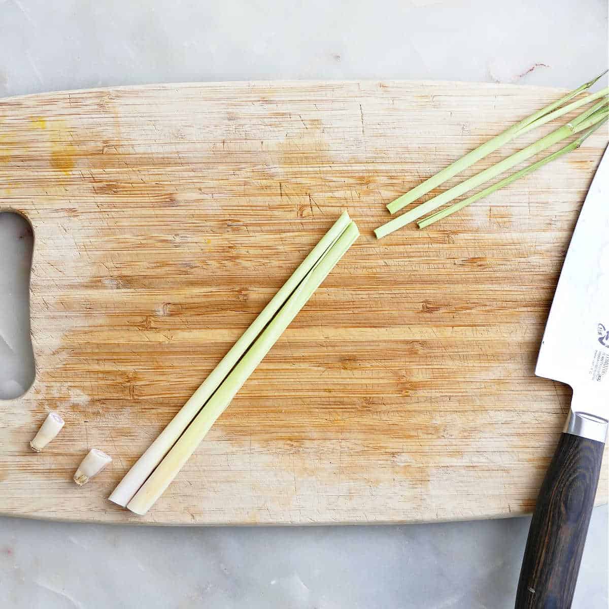 Lemongrass stalks with the top and bottom sliced off on a cutting board.