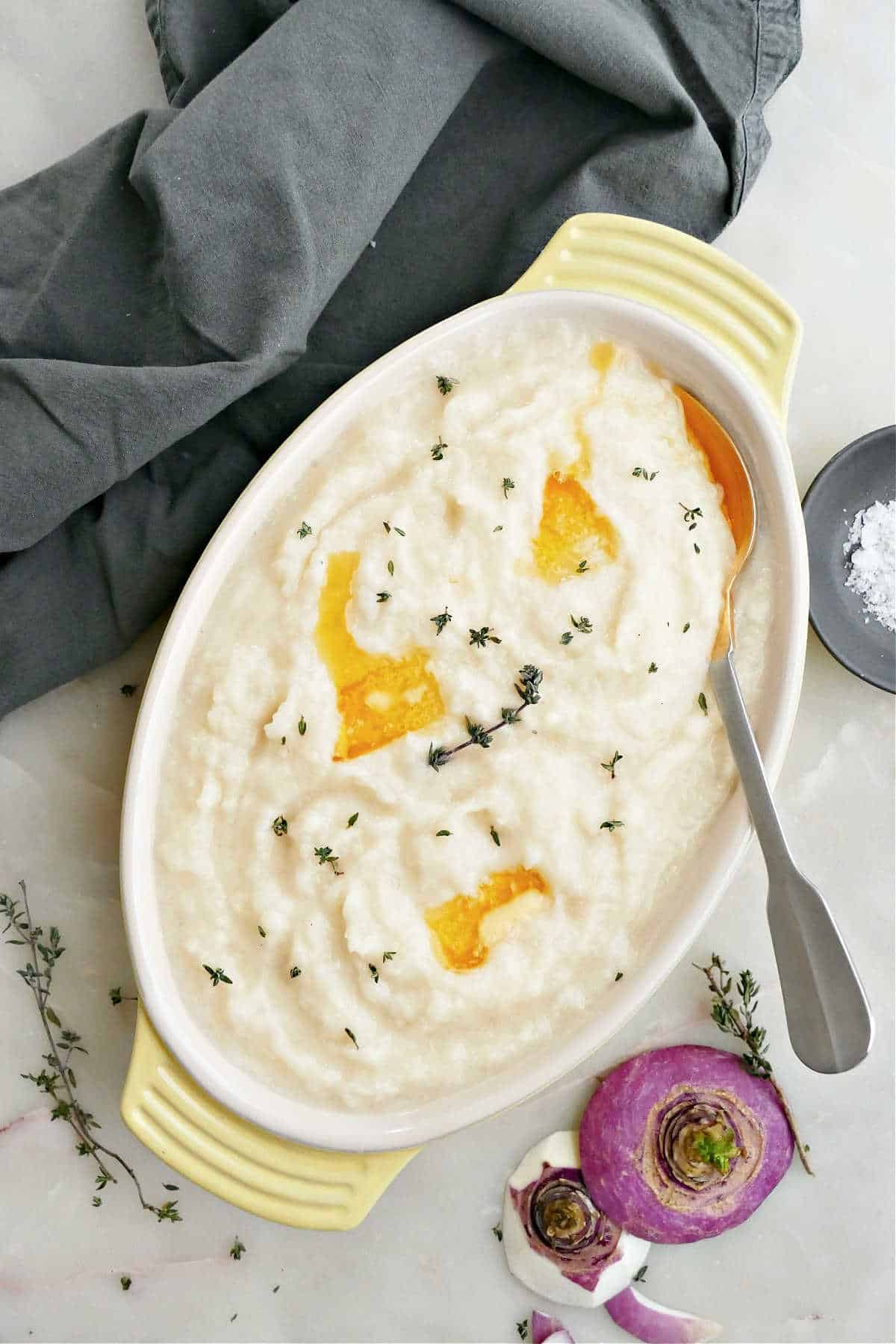 Mashed turnips with pats of melted butter and thyme in a serving dish.