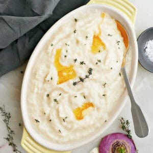 Mashed turnips with pats of melted butter and thyme in a serving dish.