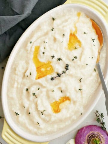 Mashed turnips with pats of melted butter and thyme in a serving dish.