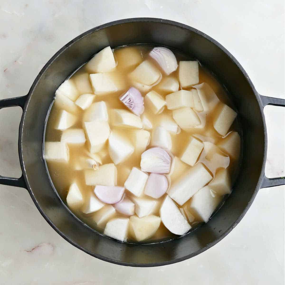 Turnips, potatoes, shallots, and garlic in a pot with broth before boiling.