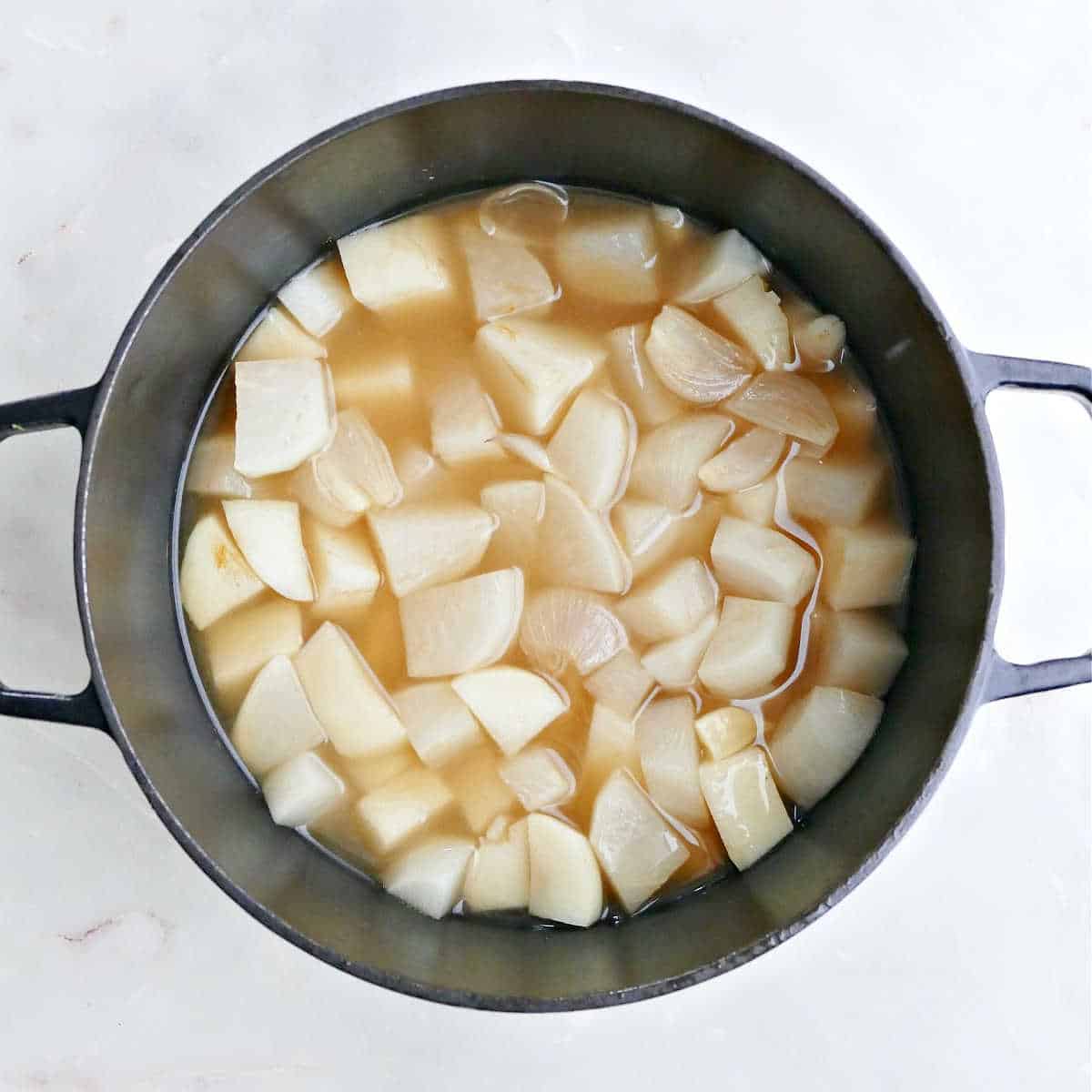 Turnips, potatoes, shallots, garlic, and broth in a pot after boiling.