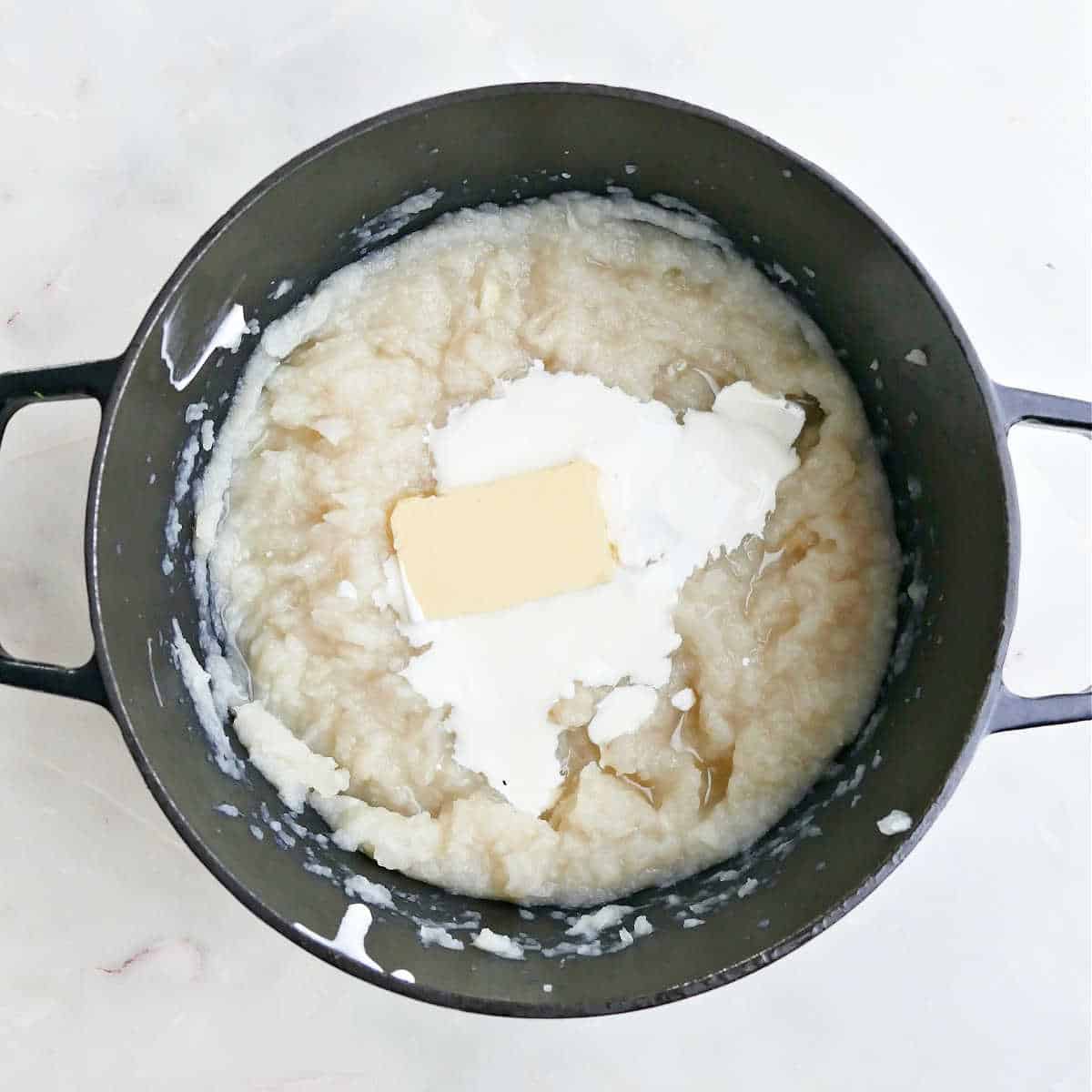 Mashed turnips with butter and sour cream being added to them in a pot.