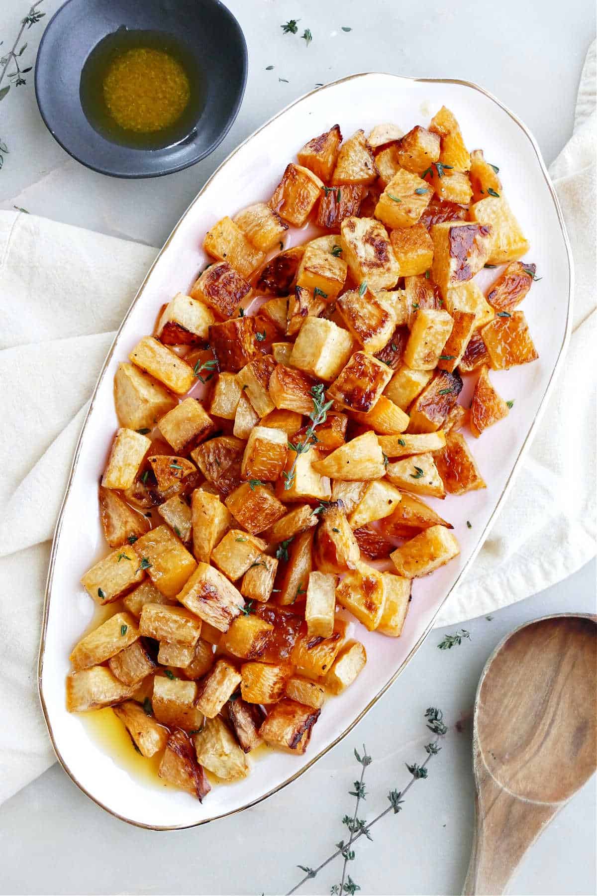 Roasted rutabaga on a serving tray next to garnishes and a spoon.