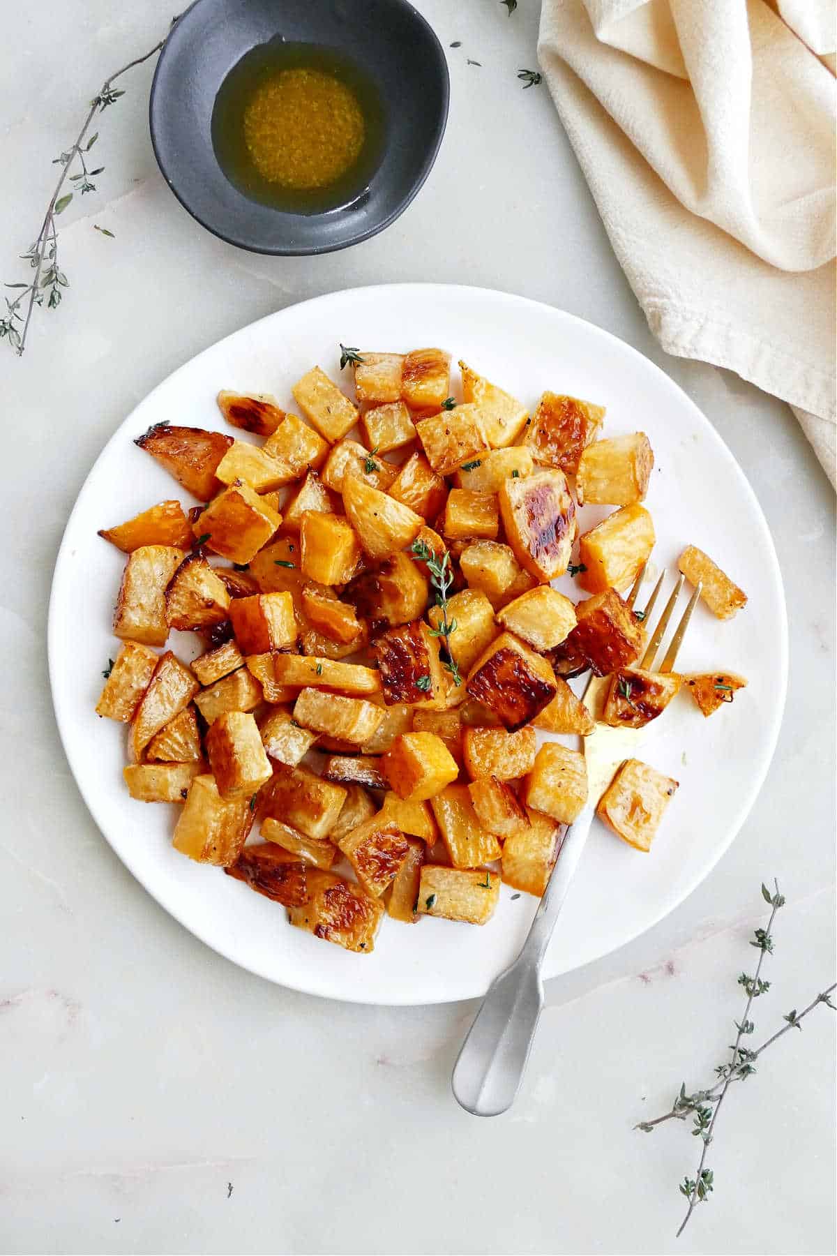 A plate of roasted rutabaga with a fork next to garnishes and a napkin.