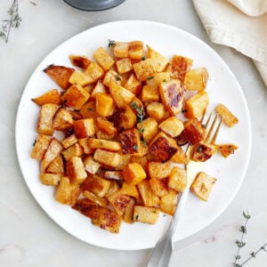 A plate of roasted rutabaga with a fork next to garnishes and a napkin.