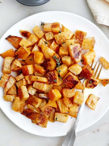 A plate of roasted rutabaga with a fork next to garnishes and a napkin.