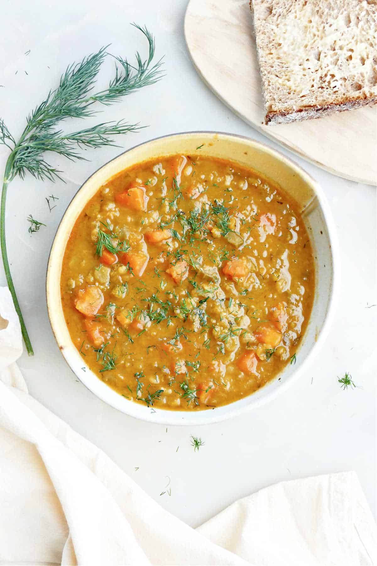 Split pea and carrot soup next to bread, dill, and a napkin.