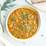 Split pea and carrot soup next to bread, dill, and a napkin.