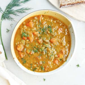 Split pea and carrot soup next to bread, dill, and a napkin.