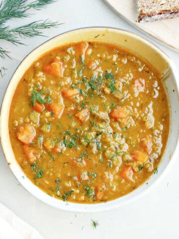 Split pea and carrot soup next to bread, dill, and a napkin.