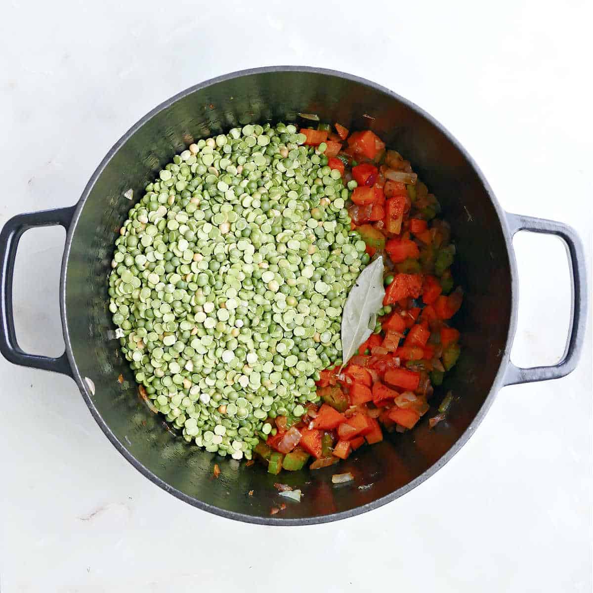 Cooked vegetables, dried split peas, and a bay leaf in a soup pot.