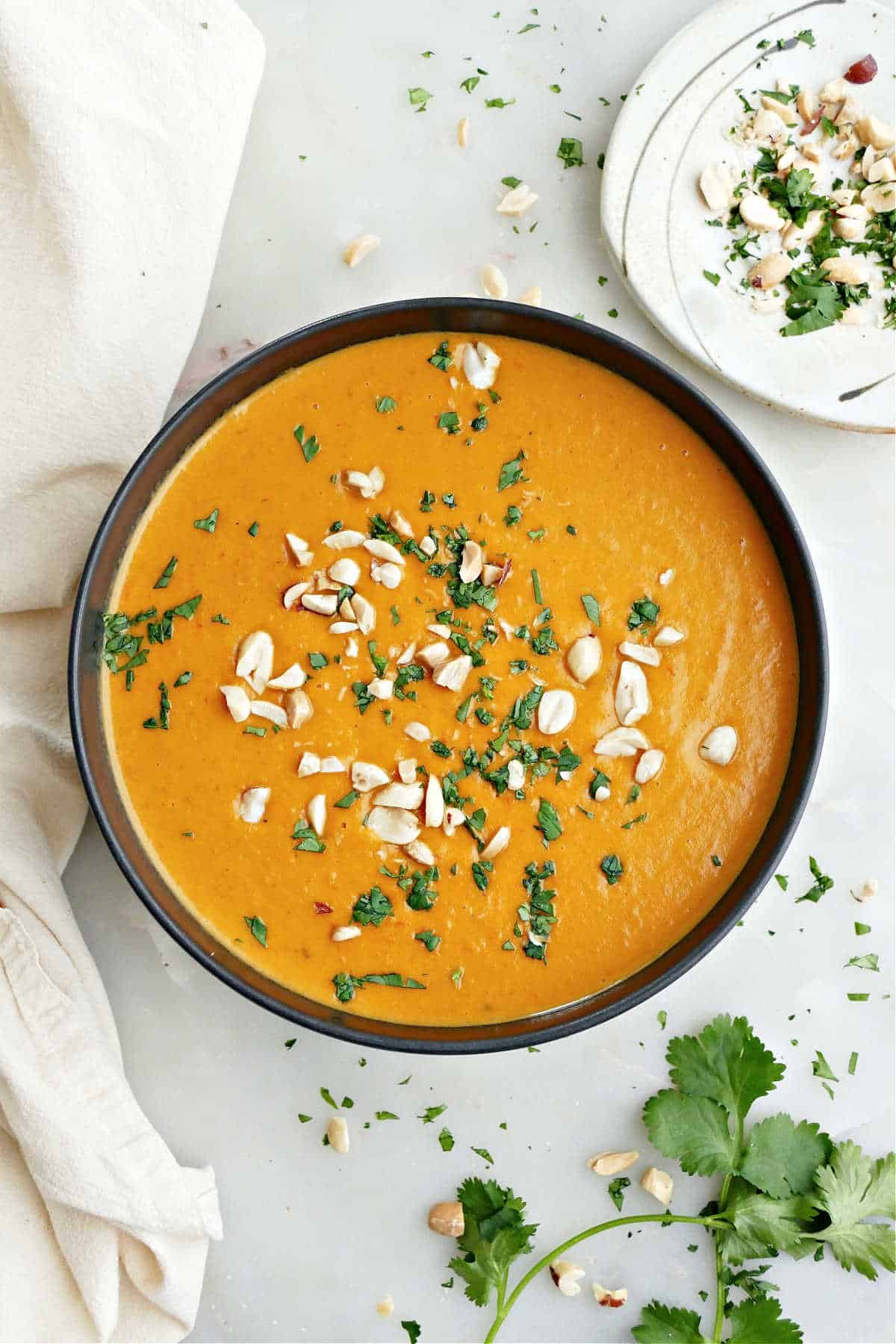 Sweet potato and red pepper soup garnished with cilantro and peanuts in a bowl.