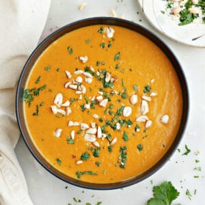 Sweet potato and red pepper soup garnished with cilantro and peanuts in a bowl.