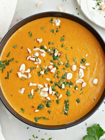 Sweet potato and red pepper soup garnished with cilantro and peanuts in a bowl.