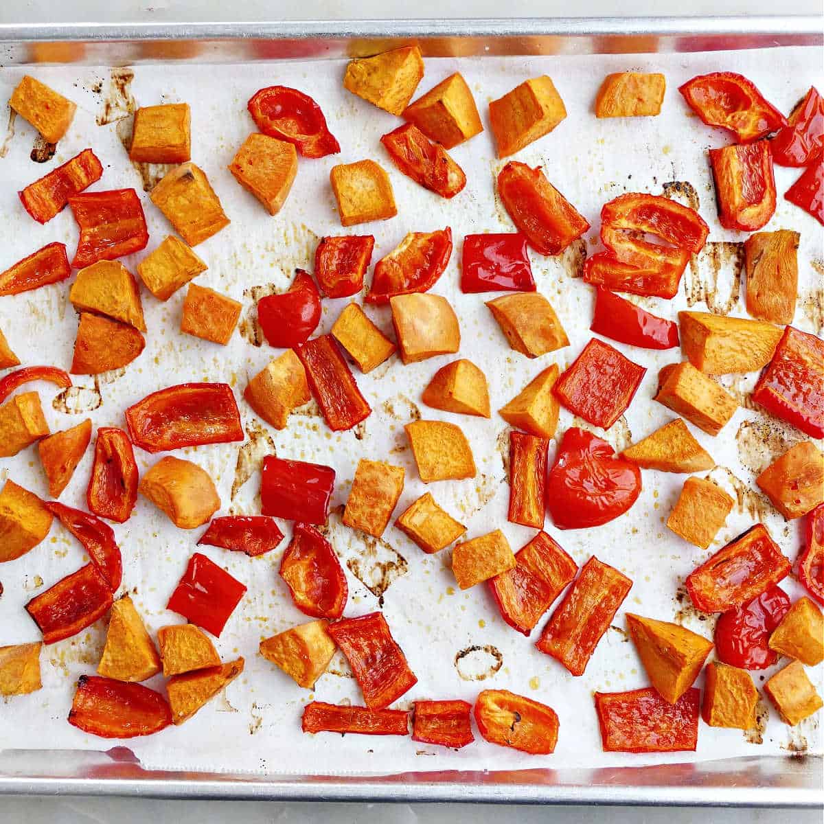 Roasted sweet potatoes and red peppers on a lined baking sheet.