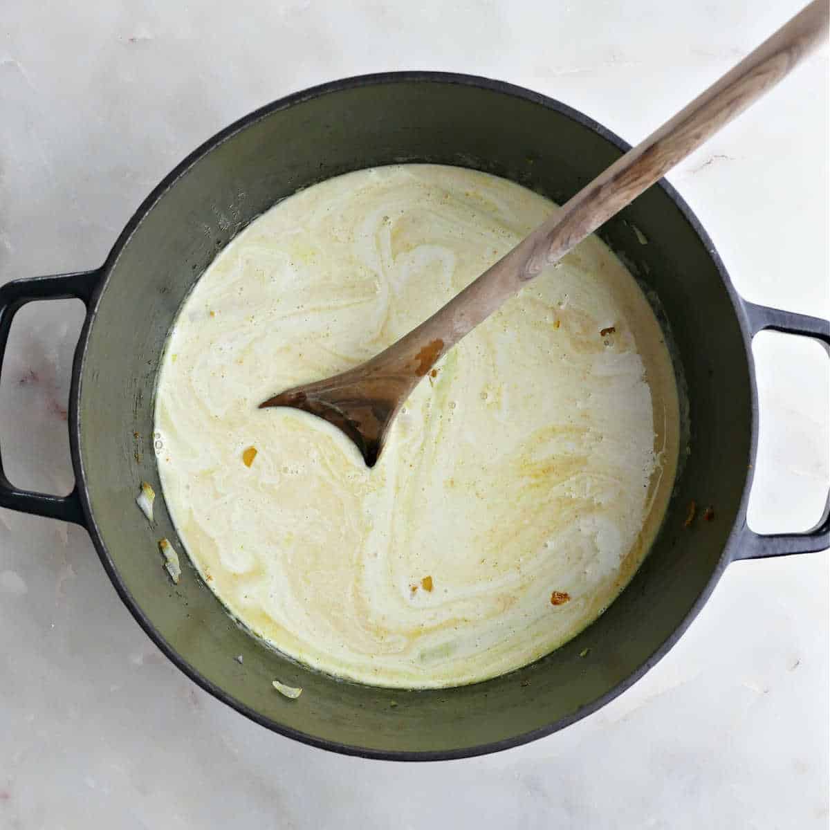 Coconut milk lemongrass broth cooking in a Dutch oven with a spoon.