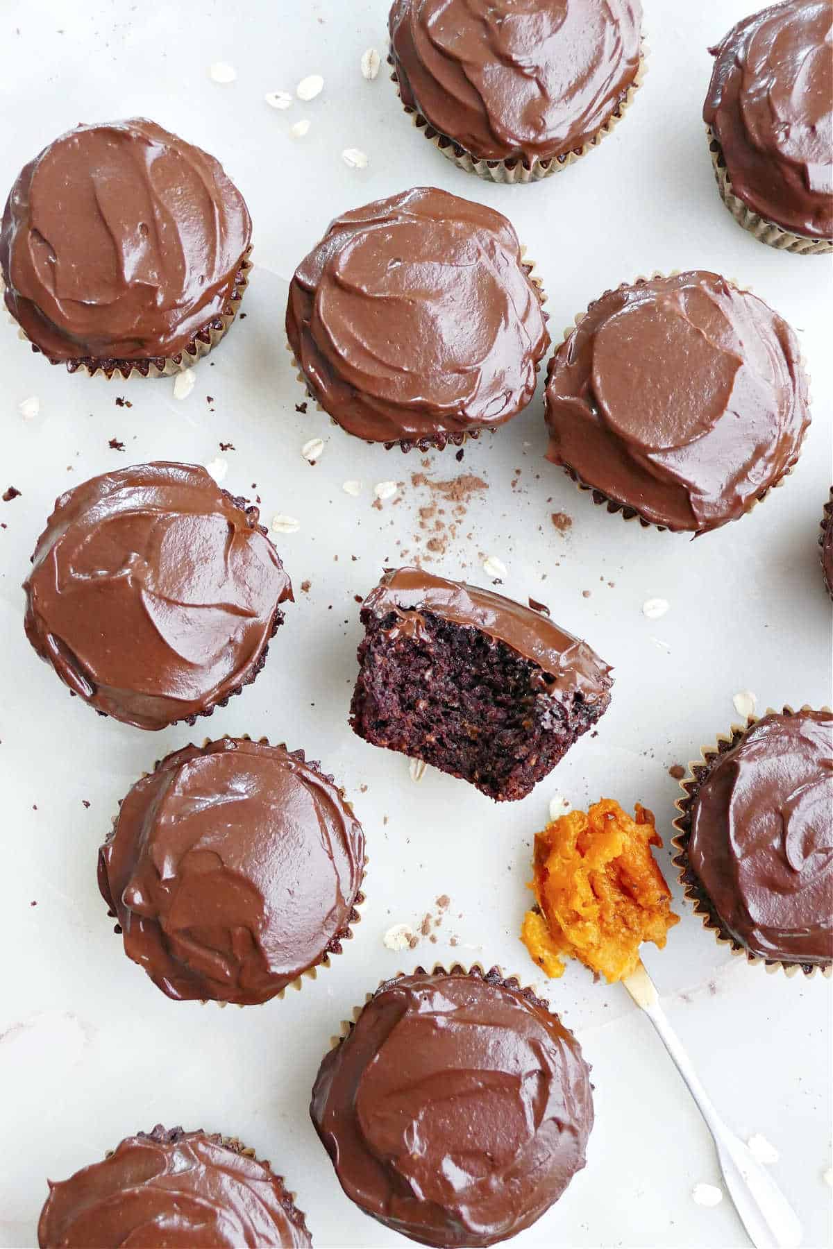 Chocolate almond flour cupcakes with avocado frosting on a counter next to spoon of sweet potato.