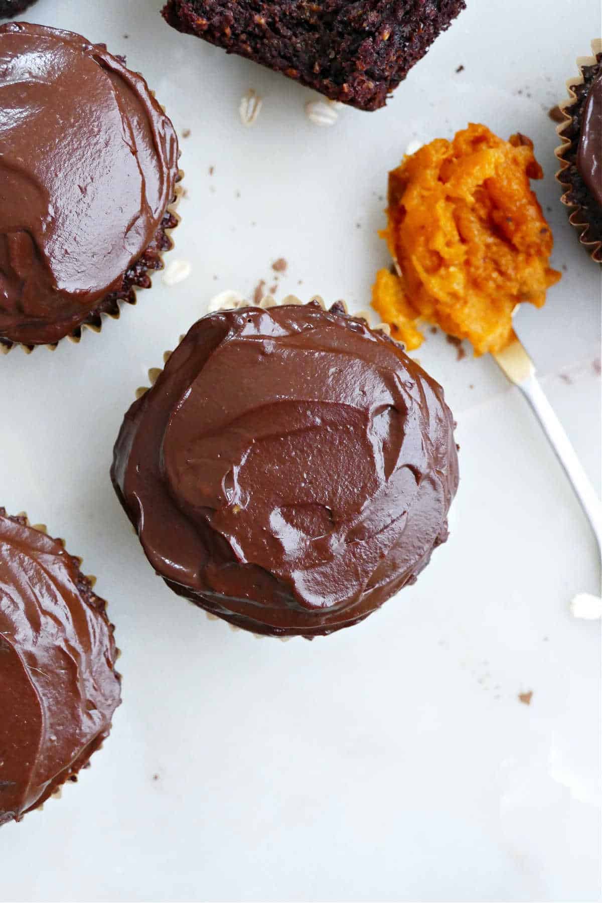 Chocolate cupcakes with avocado frosting next to sweet potato on a spoon.