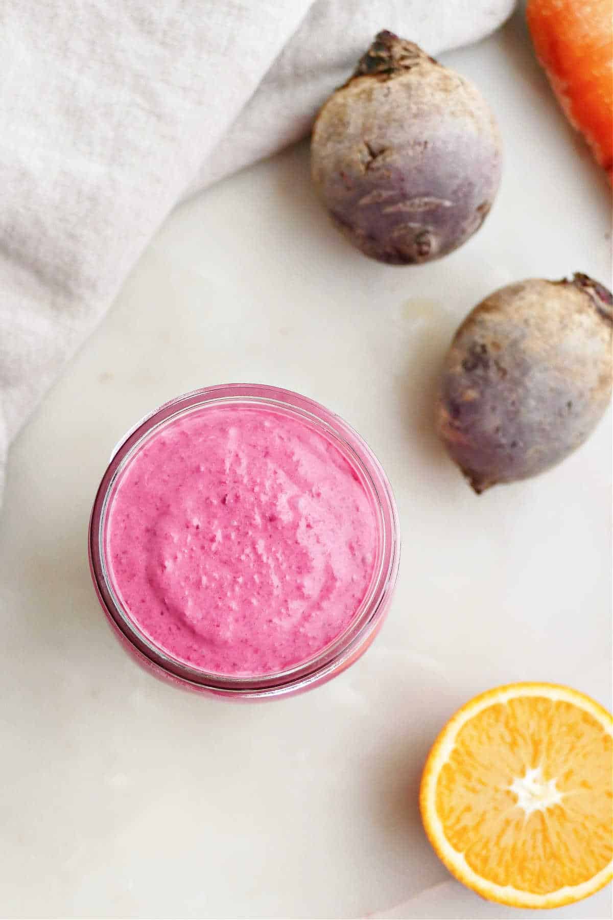 Beet smoothie next to beets, orange, carrot, and a napkin.