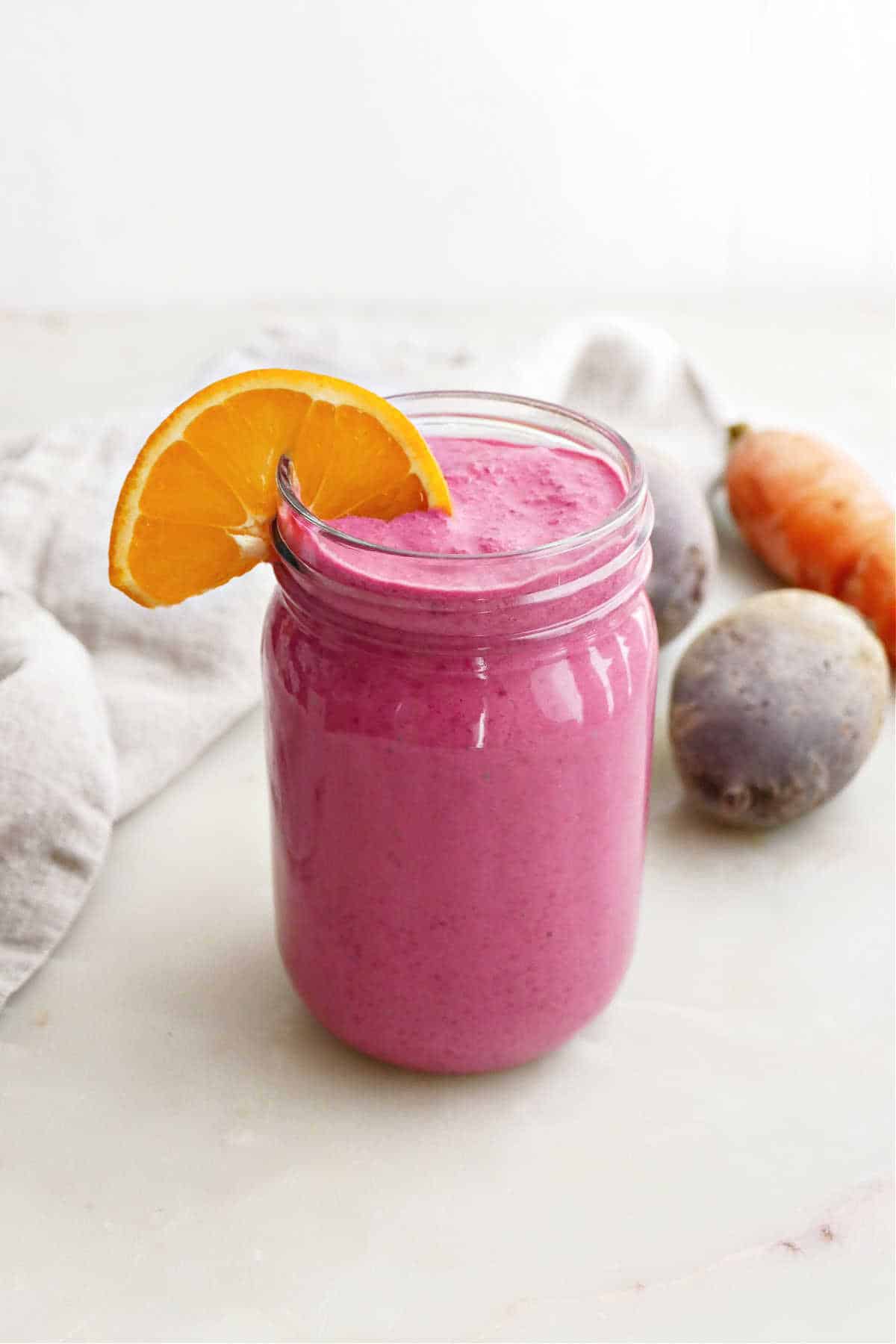 Pink smoothie made from beetroot in a glass with an orange wedge.